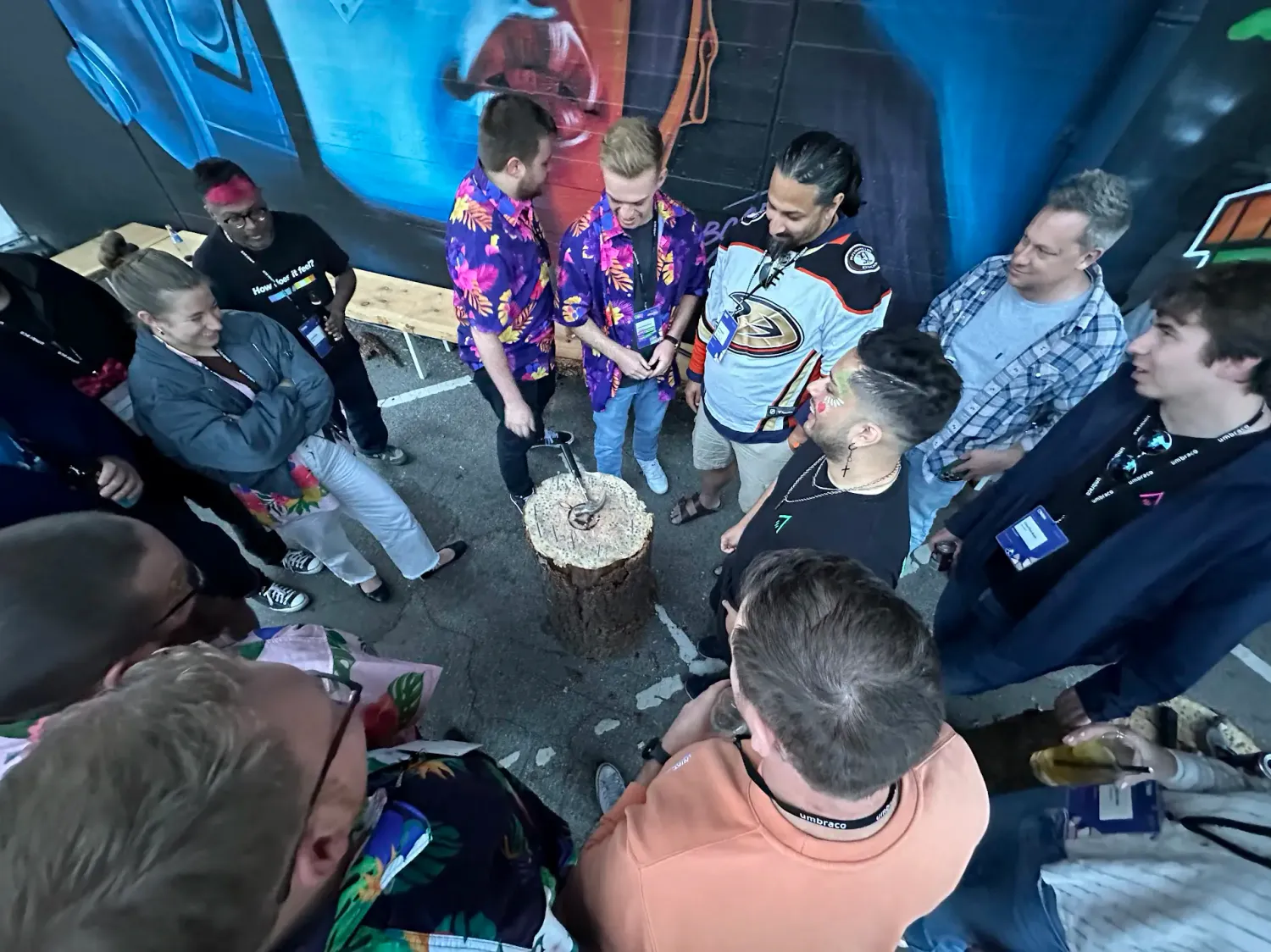 A circle of community members stood around a tree stump playing hammerschlagen